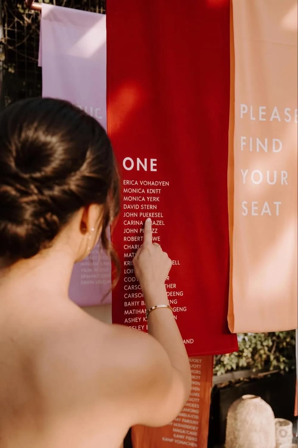 Boho seating chart fabric banners in red, coral and pink printed with table groupings, a guest reading the names