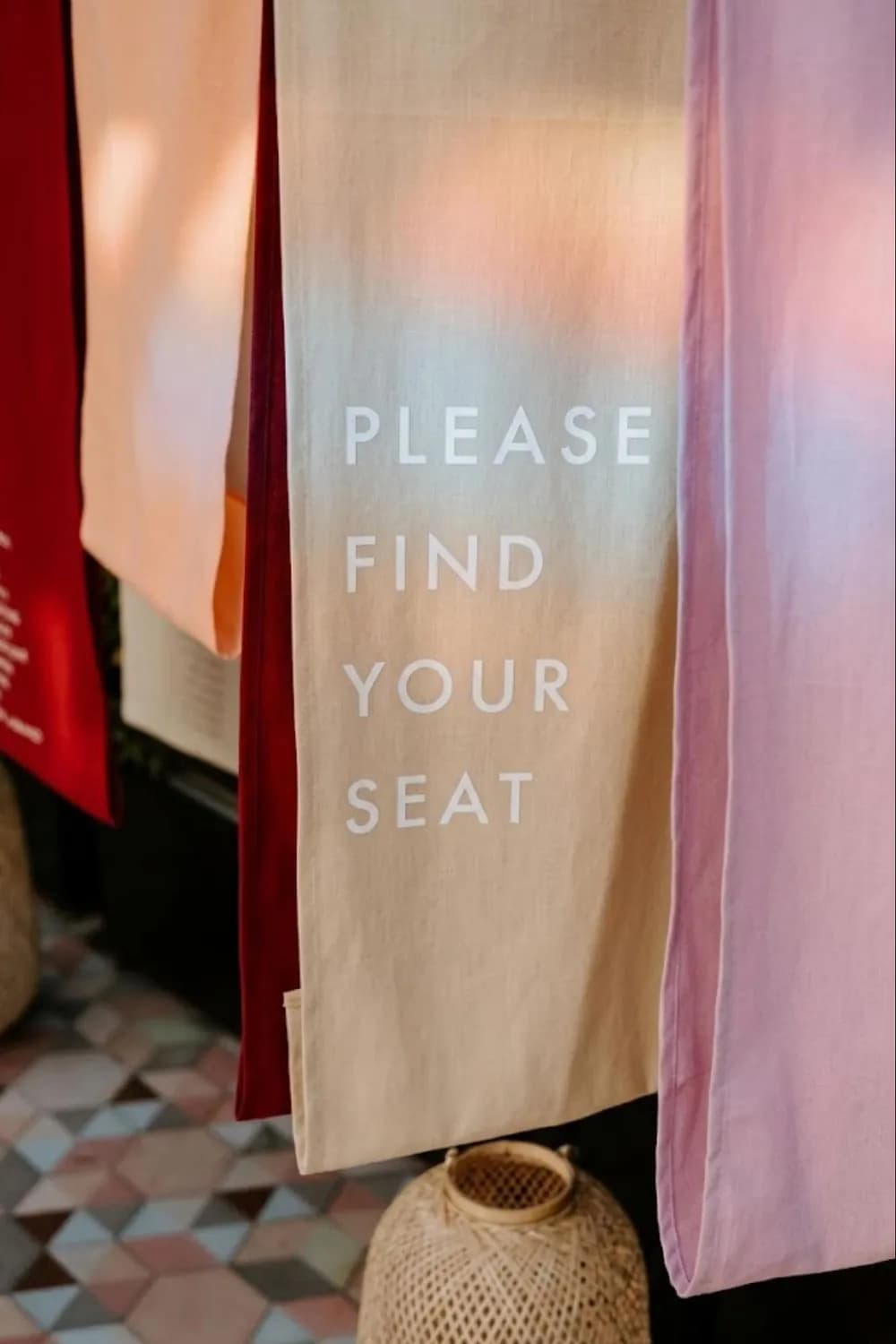 Soft peach, pink and oatmeal fabric panels printed 'Please Find Your Seat' beside a woven lantern