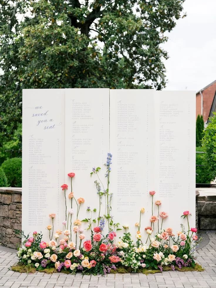 A pale 'we saved you a seat' seating board set into a low garden meadow of pink, coral and yellow blooms outdoors