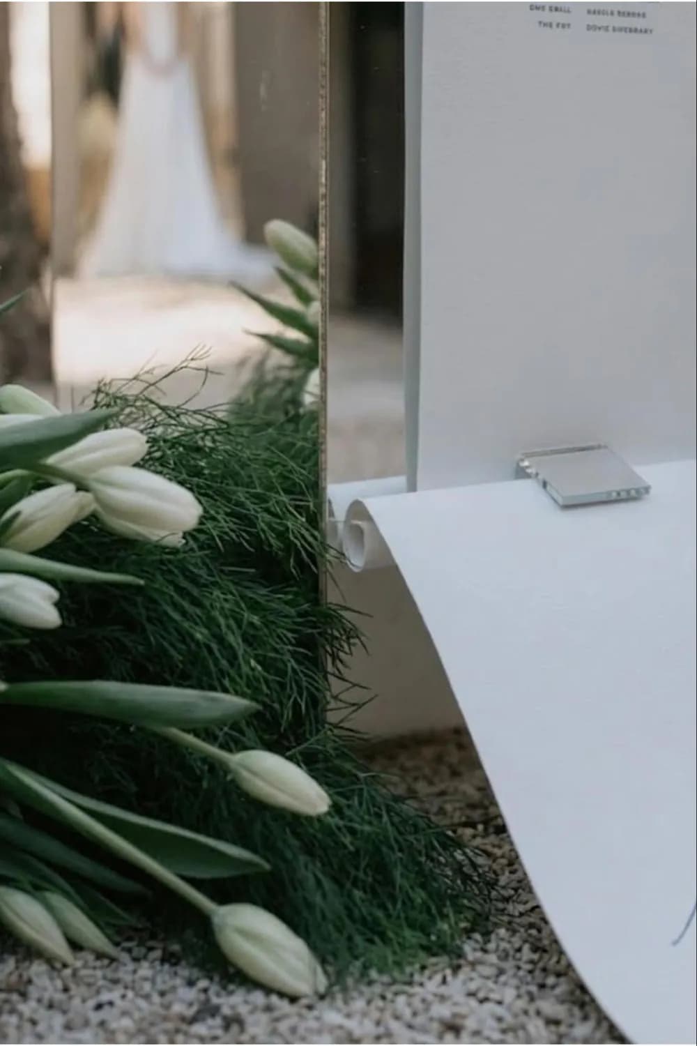A white curved seating board with calligraphy names rising from a bed of greenery and white tulips