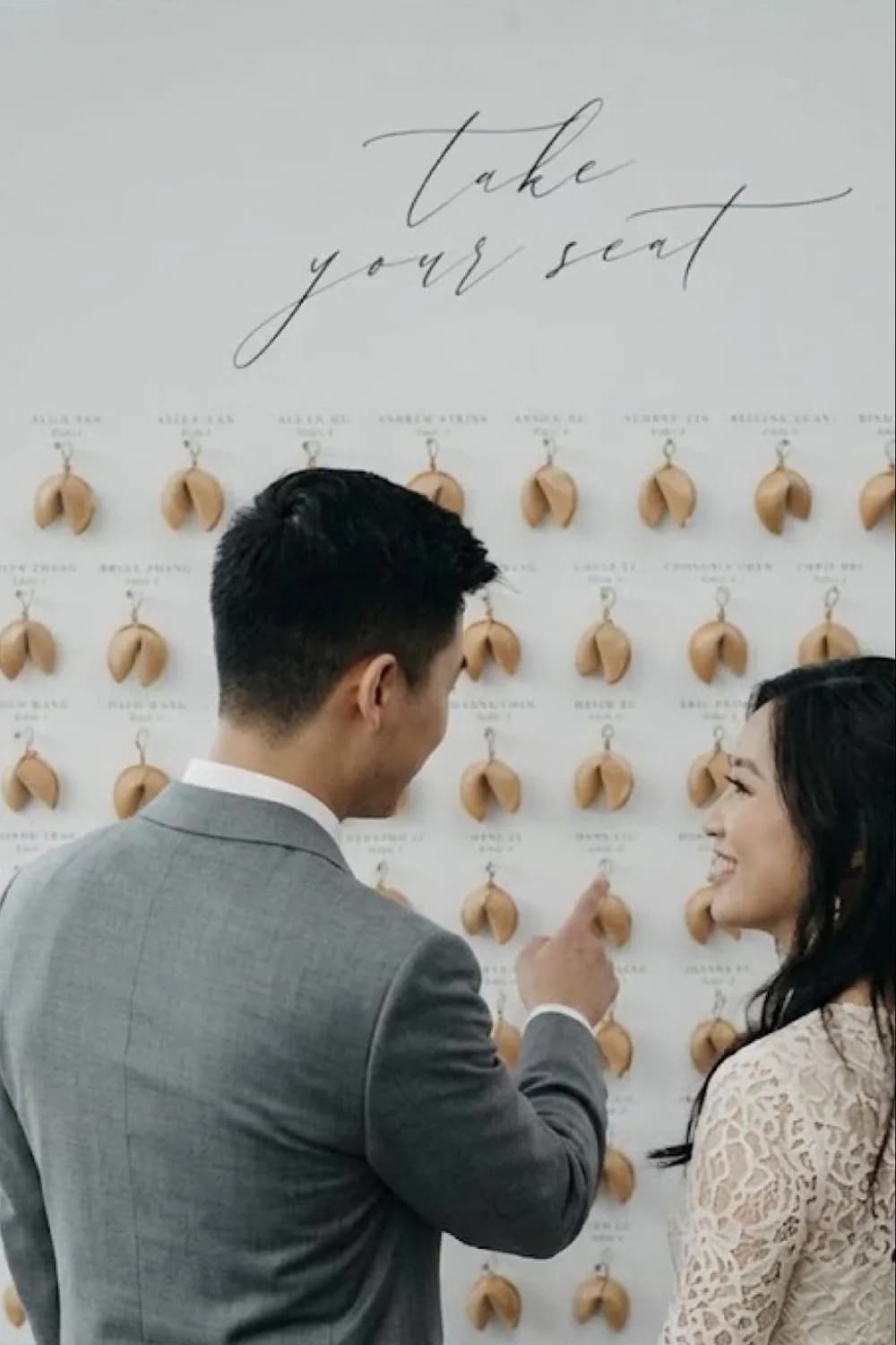 A couple finding their fortune cookie on a 'take your seat' escort-card wall and cracking it open to reveal a table number